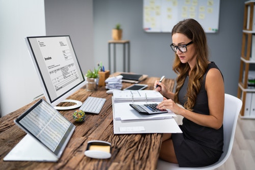 a woman at a desk with paperwork and a calculator and a computer