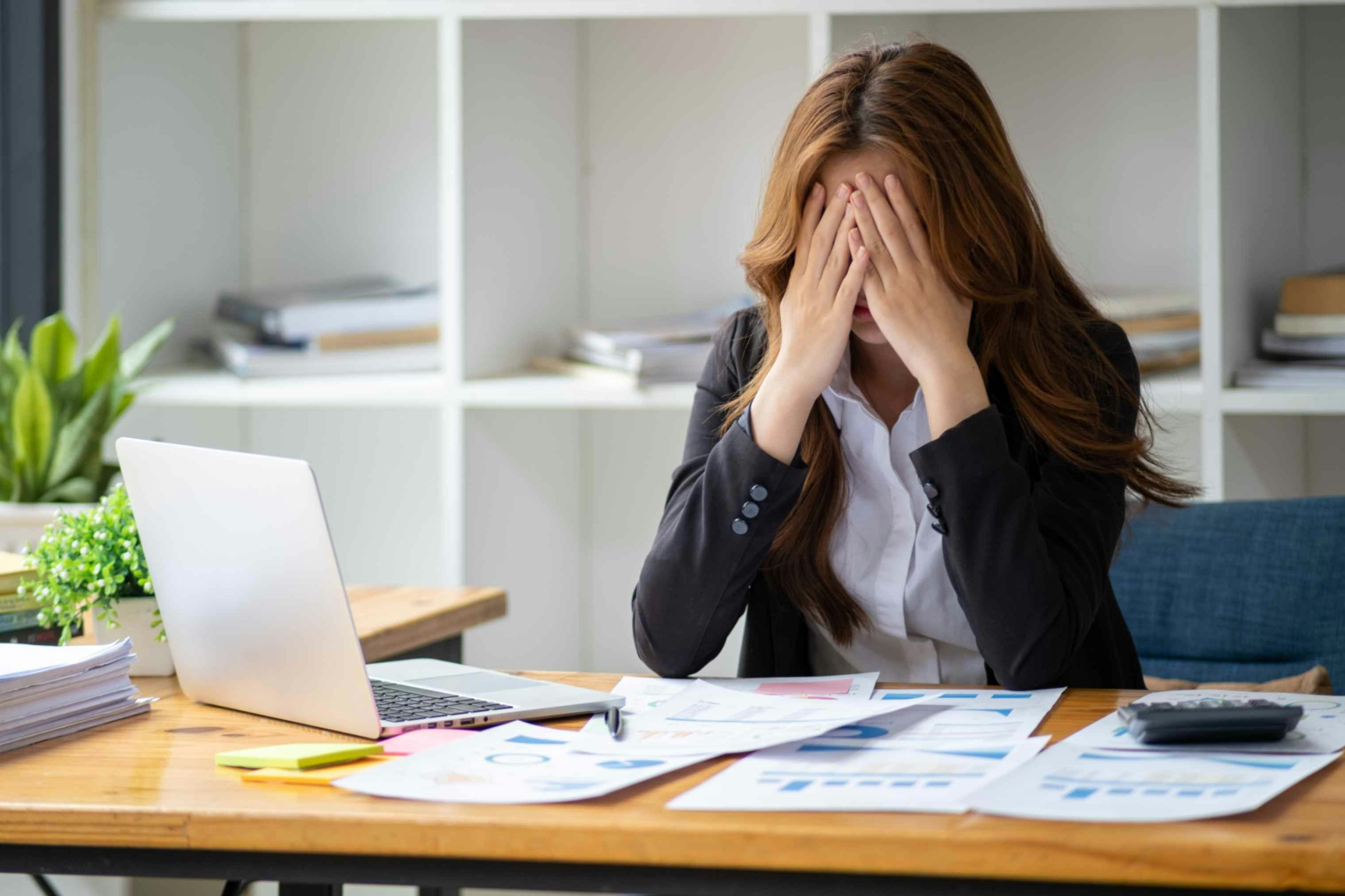 a woman at a desk in a suit with her head in her hands