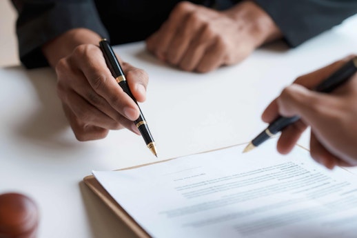 two men with pens writing on a document