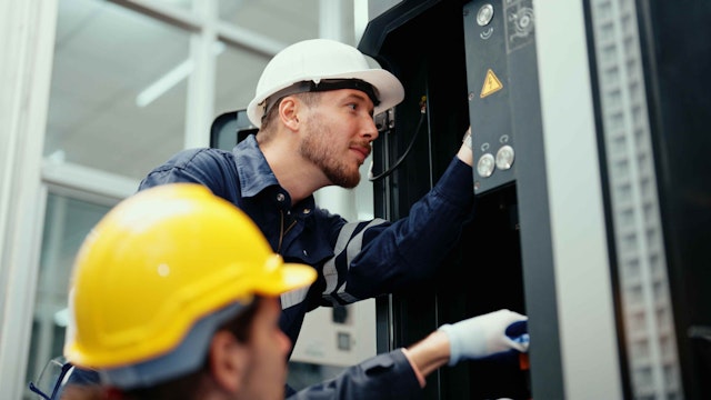 Two men in helmets looking at a piece of machinery