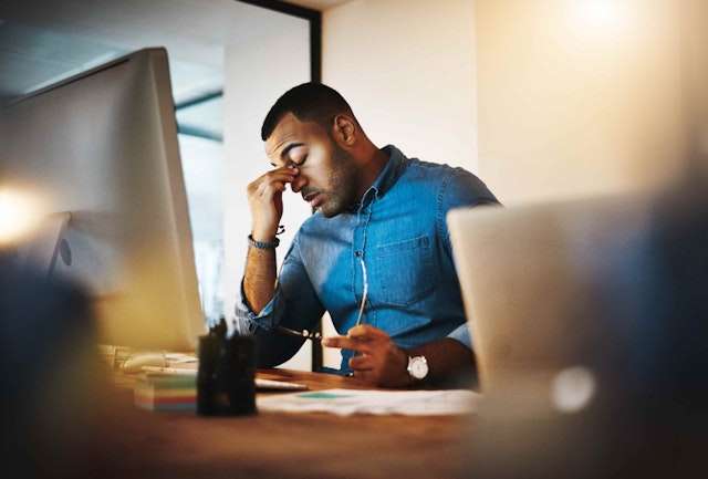 A man working at a desk holding his head in his hands