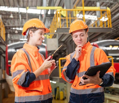 two workers in ppe in a warehouse looking at a clipboard