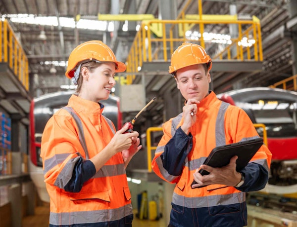 two workers in ppe in a warehouse looking at a clipboard