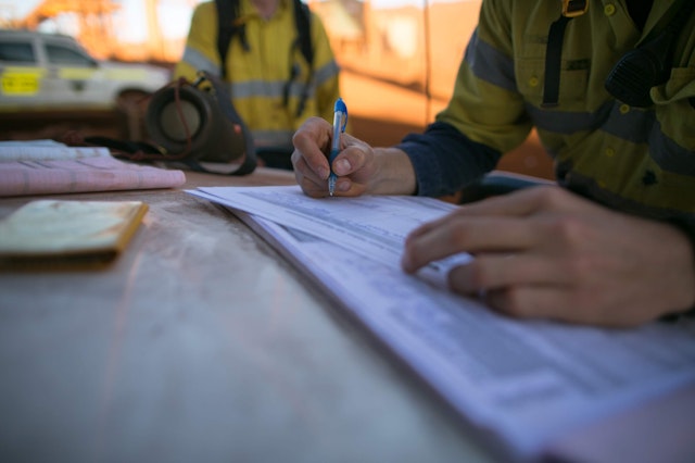 Two men in PPE filling out documentation outside work