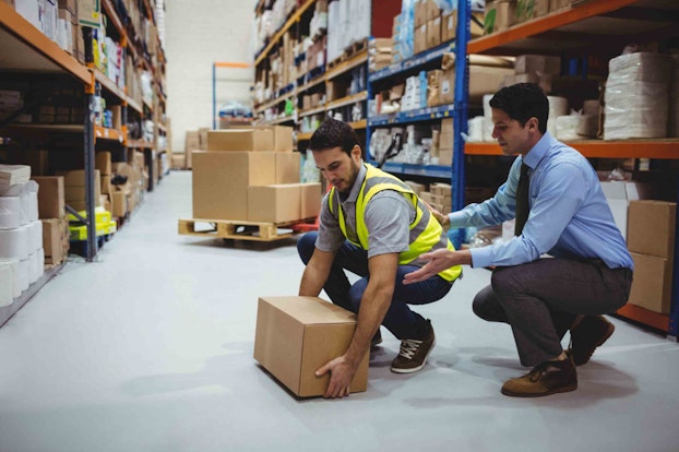 a male worker helping another worker in ppe lift a box in a warehouse