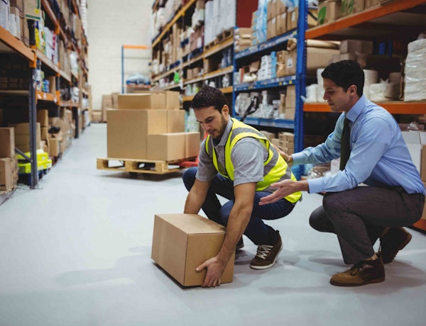 a male worker helping another worker in ppe lift a box in a warehouse