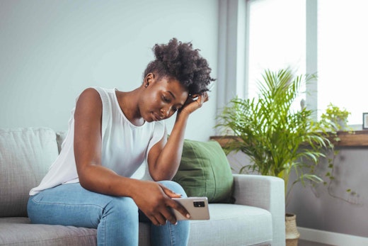 a woman on her phone holding her head on a couch