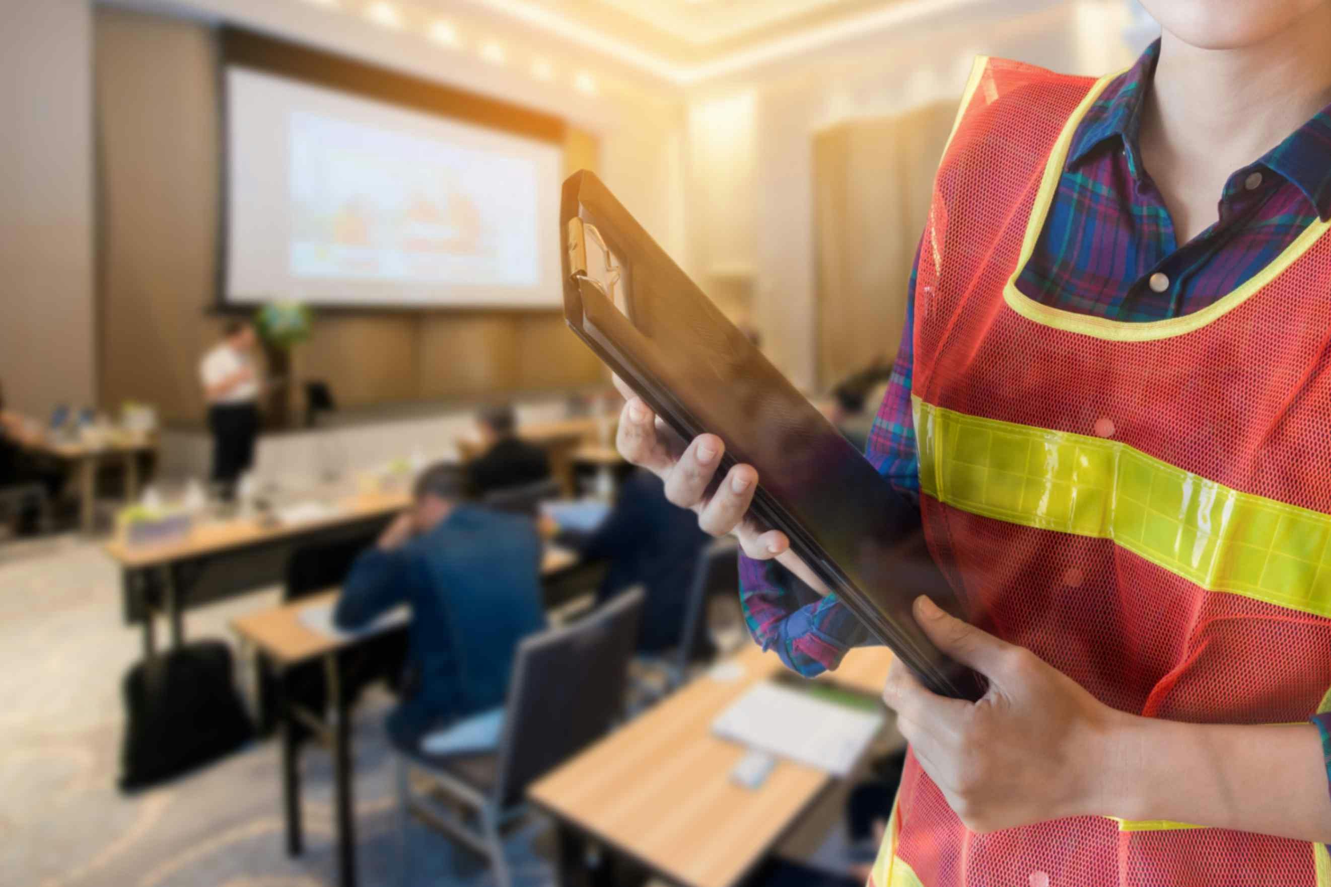 a woman in ppe holding a clipboard as people work behind her