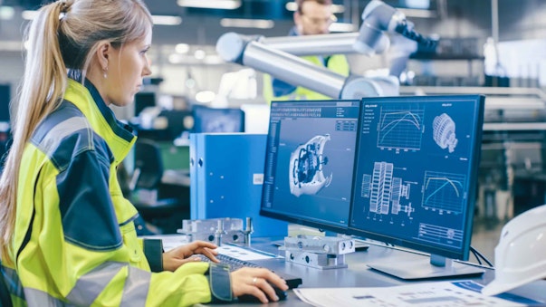 a woman in a high vis jacket looking at two computer screens