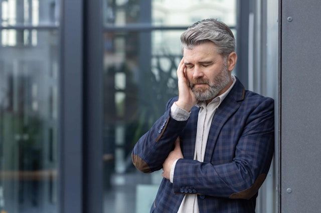 A man stood outside a building in formal wear holding his head