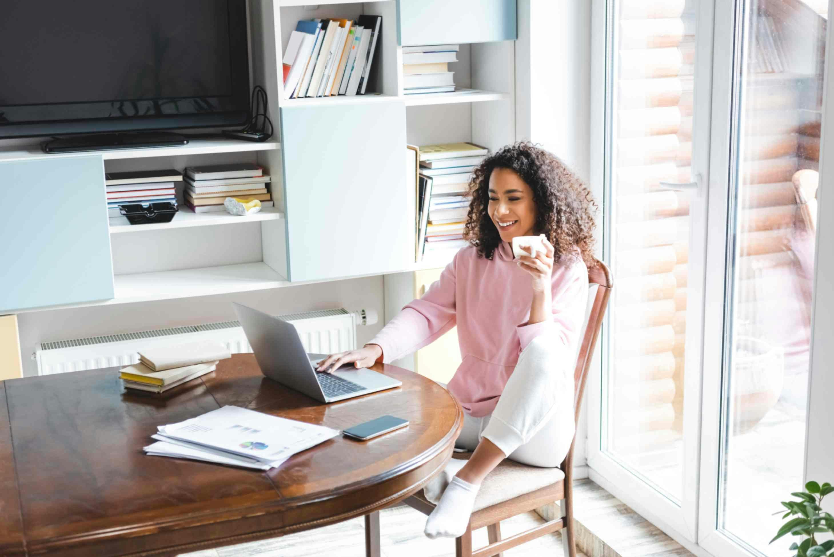 A woman sat at a kitchen table with a laptop smiling