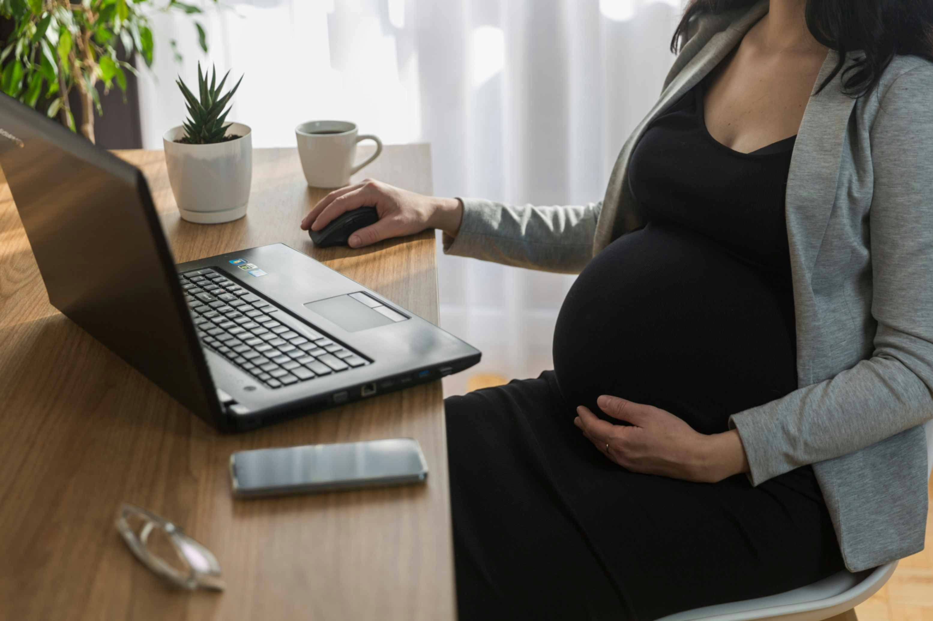 A pregnant employee at her desk with her laptop and phone.