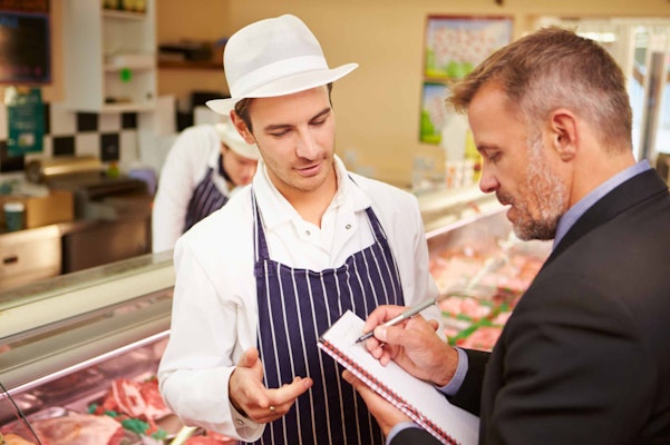 two men speaking whilst one writes on a notepad at a butchers