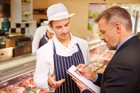 two men speaking whilst one writes on a notepad at a butchers