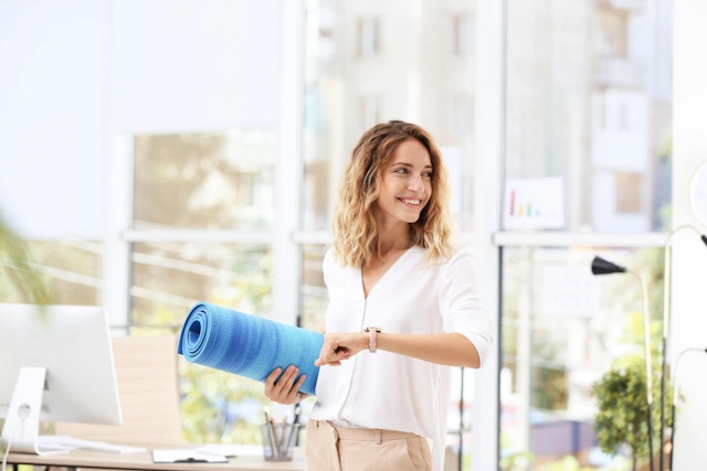 a woman in an open office smiling holding a yoga mat