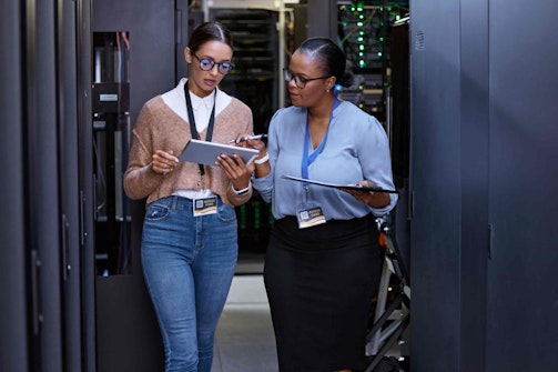 two women standing in a hallway looking at tablets