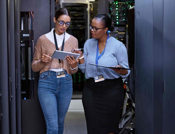 two women standing in a hallway looking at tablets