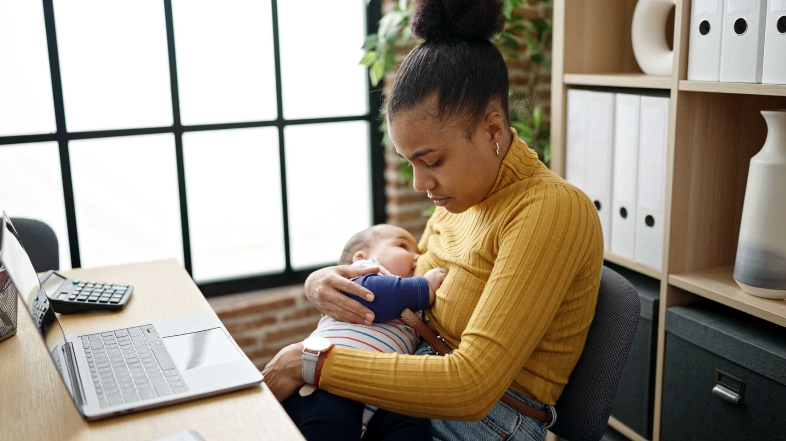 A woman sat at a laptop breastfeeding a baby