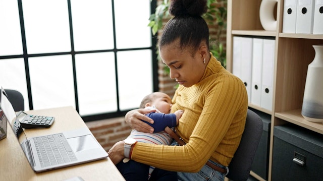 A woman sat at a laptop breastfeeding a baby