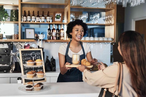 A cafe worker handing food and drink to customer smiling