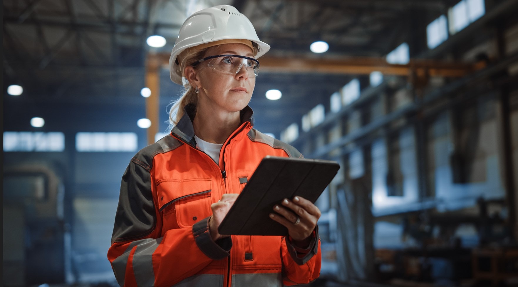 a woman holding a clipboard in a warehouse with PPE on