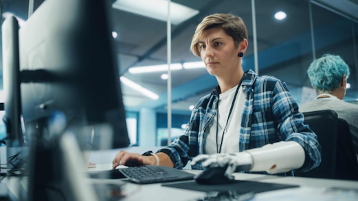 A woman with a prosthetic arm typing at a computer