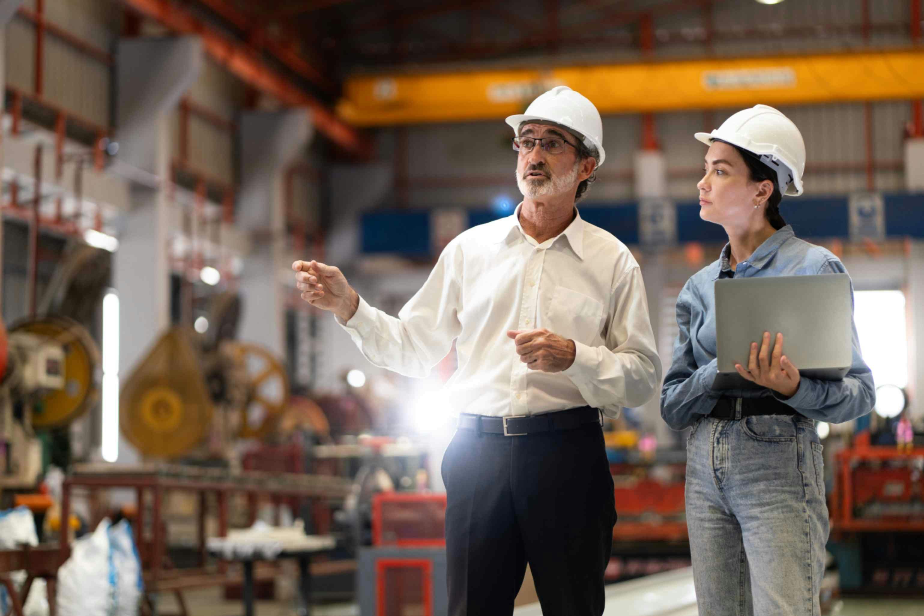 a man and woman in hard hats in a warehouse looking at computer