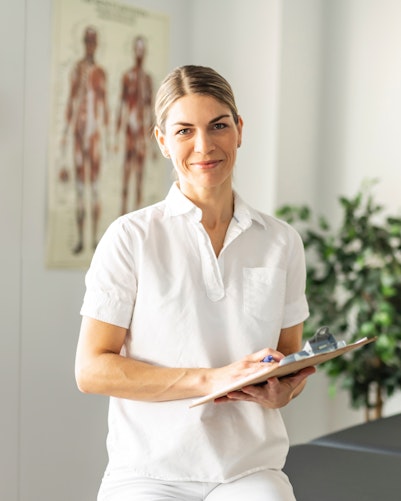 Woman in medical office smiling and holding clipboard