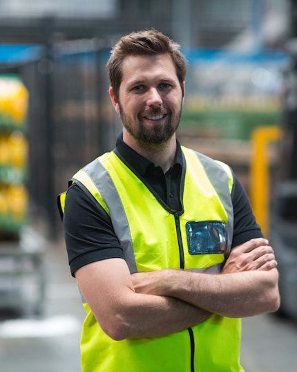 Man in industrial setting smiling with arms folded