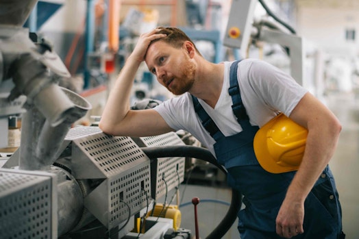 man holding his head and leaning on workplace equipment