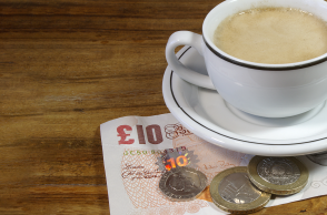 cup of coffee sat on top of ten pound note and pound coins