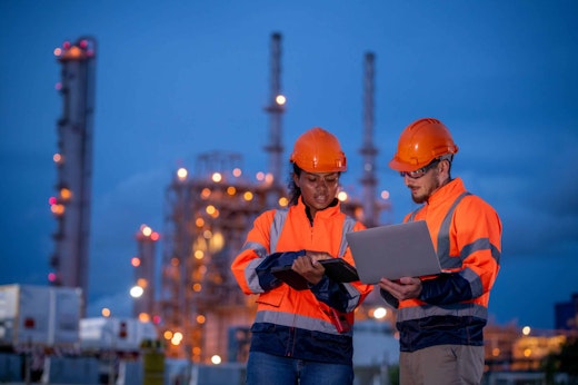 a man and woman in hard hats outside warehouse looking at computer