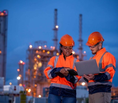 a man and woman in hard hats outside warehouse looking at computer