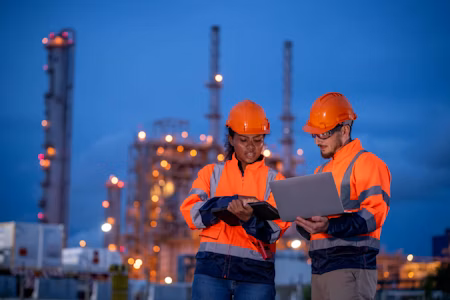 a man and woman in hard hats outside warehouse looking at computer