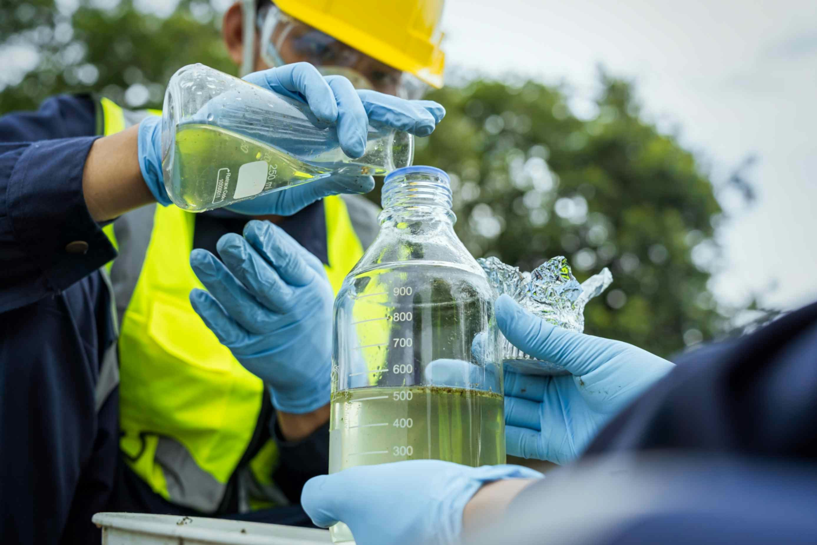 A man in ppe pouring liquid into a glass bottle