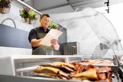 a man standing in front of meat with a clipboard