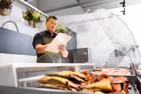 a man standing in front of meat with a clipboard