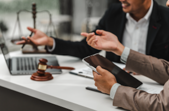 two office workers holding a laptop and tablet. A gavel is placed on the table.