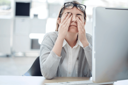 woman rubbing her eyes at her desk