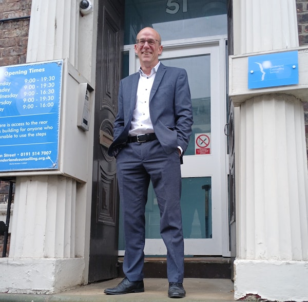 A man wearing a suit standing outside the entrance of a building,