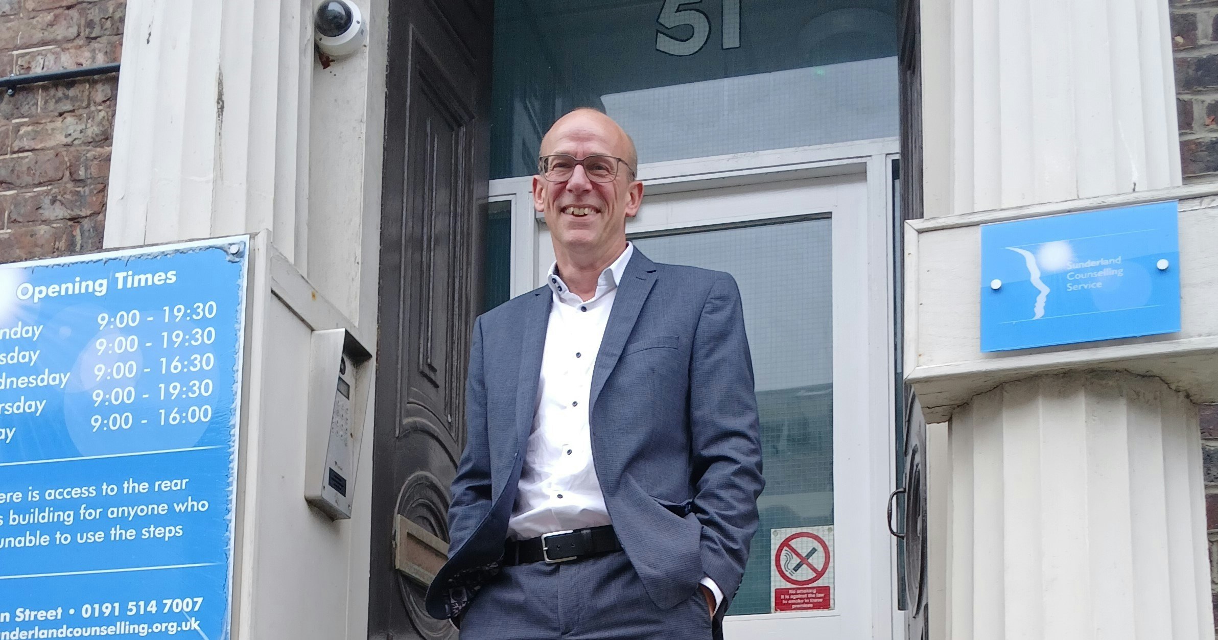 A man wearing a suit standing outside the entrance of a building,