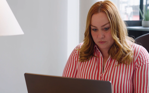 A woman wearing a striped shirt looking at a laptop.