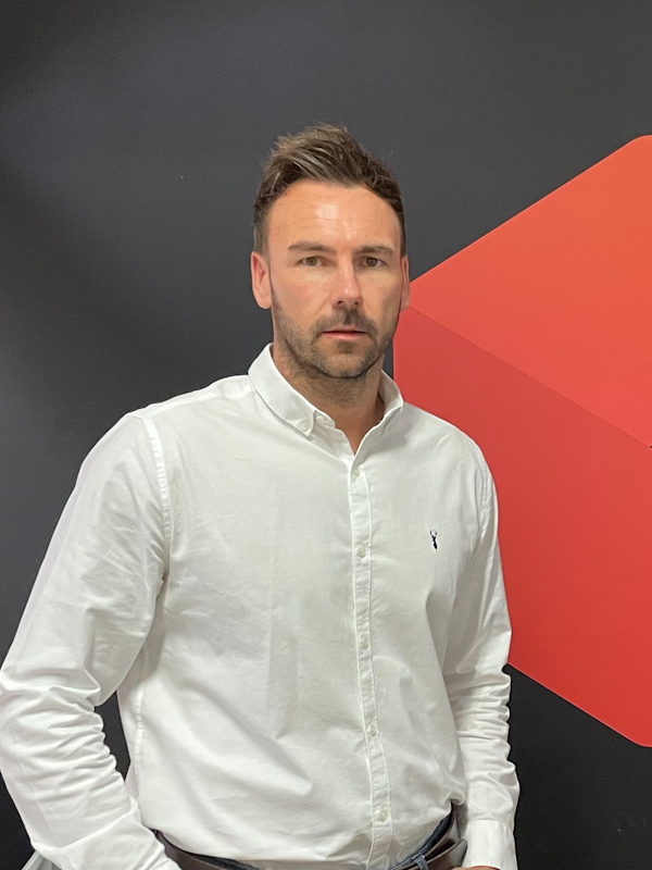 A man wearing a white shirt against a black wall.