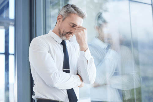 A stressed man in formal attire standing close to a meeting room window