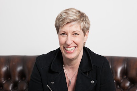 A woman is sat on a leather sofa, smiling.