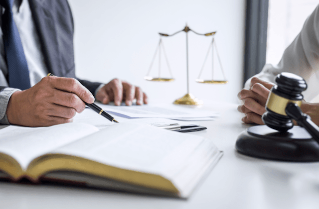 hand holding pen, a book and gavel in foreground