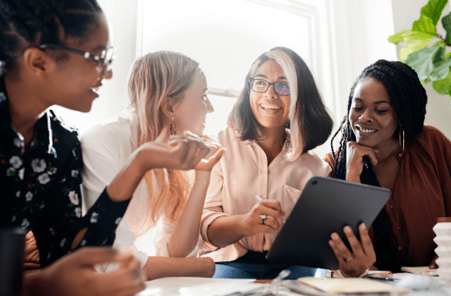 a group of women sat discussing work, one holds a tablet
