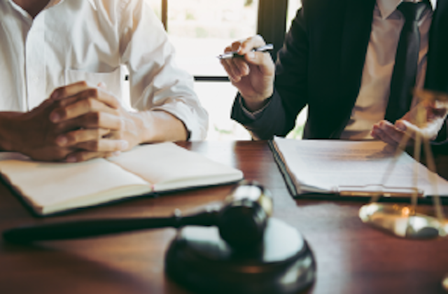 two people at a desk with notepads and pens, gavel sits in front