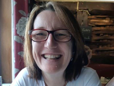A smiling woman wearing red framed glasses.