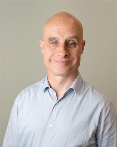 A smiling man wearing a pale blue shirt.